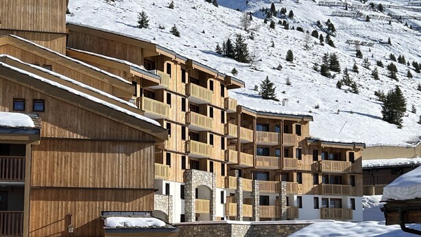 Un immeuble en bois à plusieurs étages, doté de balcons, se dressant sur fond de montagnes enneigées.