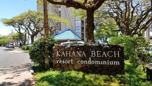 Letrero del condominio turístico KAHANA BEACH con un muro de piedra y vegetación.