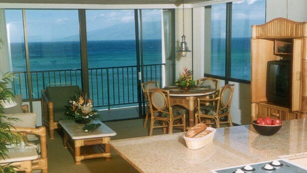Un balcón con vista al océano, un comedor con sillas y una mesa, y una cocina con estufa y un cuenco de fruta.