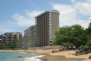 A beachfront hotel with multiple floors, a sandy beach, and palm trees.