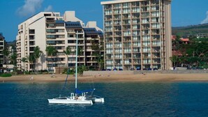Un hotel frente a la playa con varios pisos, una playa en primer plano y un barco en el agua.