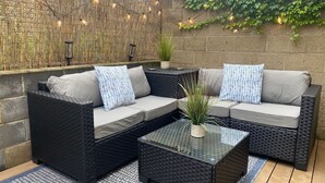 An outdoor seating area with wicker furniture, a glass coffee table, and decorative string lights. - ★ HostWise Stays ★ Spacious Stay in Prime Location | Theater & Patio (Pittsburgh)