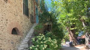 Un bâtiment en pierre avec un escalier menant à une porte, le tout entouré de verdure et d’arbres.