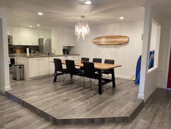 A modern kitchen with white cabinets, stainless steel appliances, and a wooden dining table with black chairs. - Cozy condo for rent 3 minutes from the beach! (San Clemente)