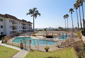 A swimming pool surrounded by a fence, with palm trees and a view of a building in the background.