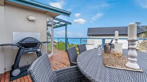 Una terrazza esterna con tavolo e sedie, un barbecue e vista sull'oceano.