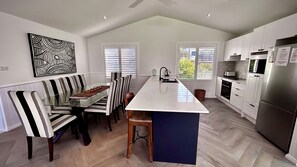 A modern kitchen with a central island, white cabinetry, and a dining area with striped chairs.