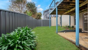 A backyard with a well-maintained lawn, a metal fence, and a covered patio area.