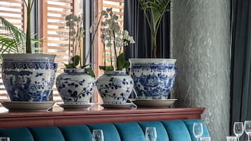 Interior de restaurante con asientos tapizados en azul, sillas de madera y grandes jarrones azules y blancos sobre una mesa central.