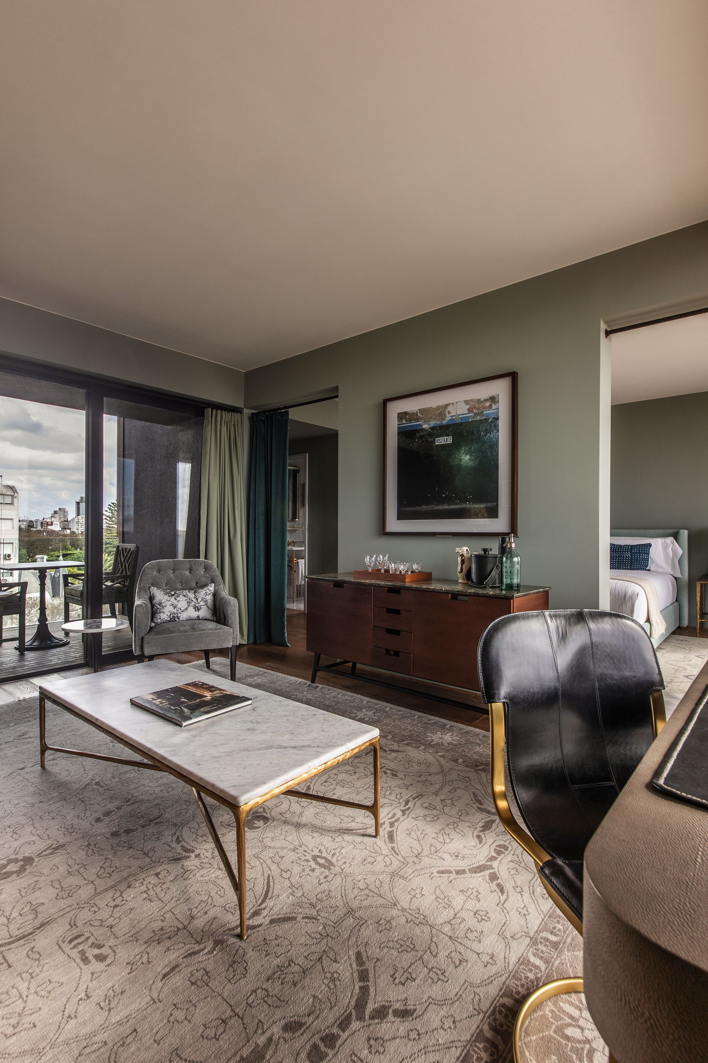 A modern hotel room with a large window, a dining table, a sofa, a desk, and a bed.