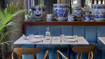 Een restaurant met een blauwe bank, houten stoelen, marmeren tafels en blauw-witte vaasjes.