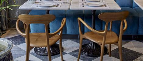 A restaurant with a blue sofa, wooden chairs, marble tables, and blue and white patterned vases.