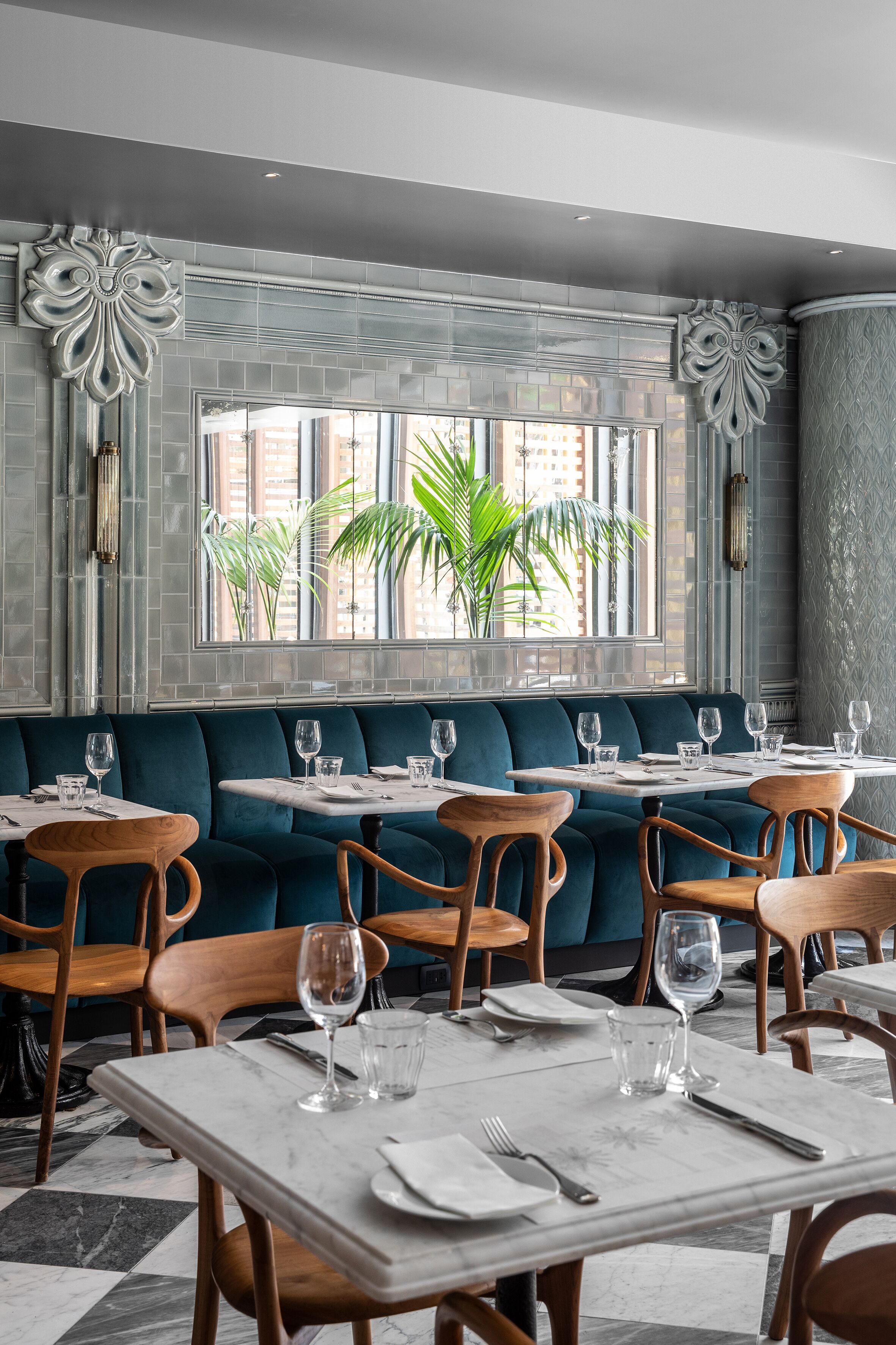 Un restaurante con una decoración moderna, que presenta una combinación de muebles de mármol y madera, un ventanal con vista a palmeras y una pared con un diseño llamativo.