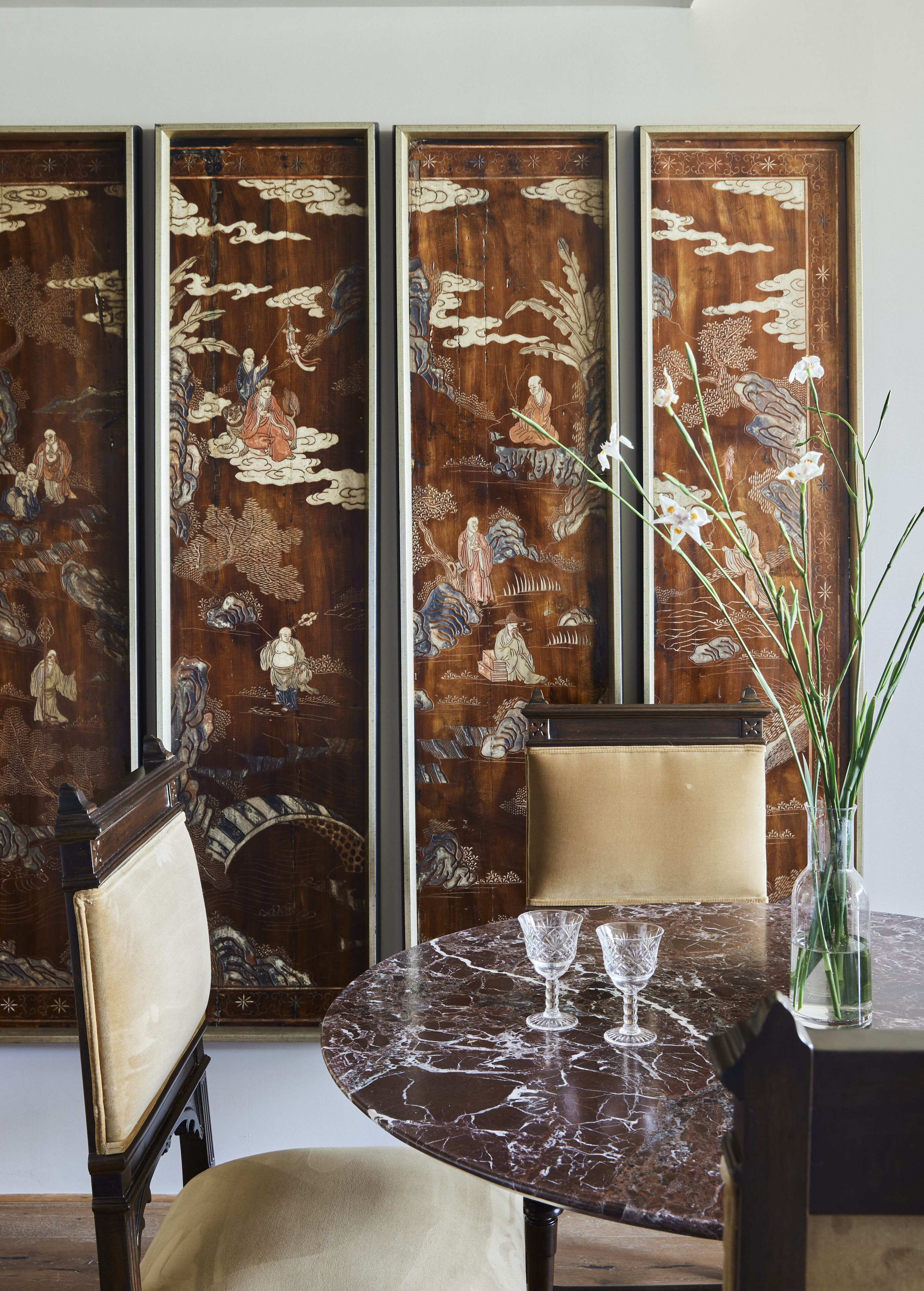 Una mesa de comedor con cubierta de mármol, rodeada de sillas, y un panel decorativo con motivos artísticos tradicionales al fondo.