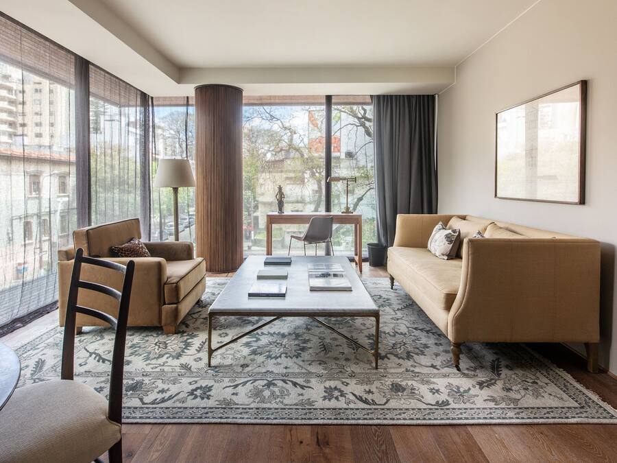 A modern living room with a sofa, armchair, coffee table, and a view of the city through large windows.