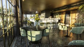 Un interior modern amb zona de bar, taules rodones i cadires verdes.