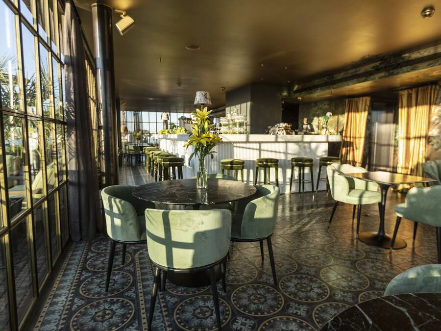 Un interior modern amb zona de bar, taules rodones i cadires verdes.
