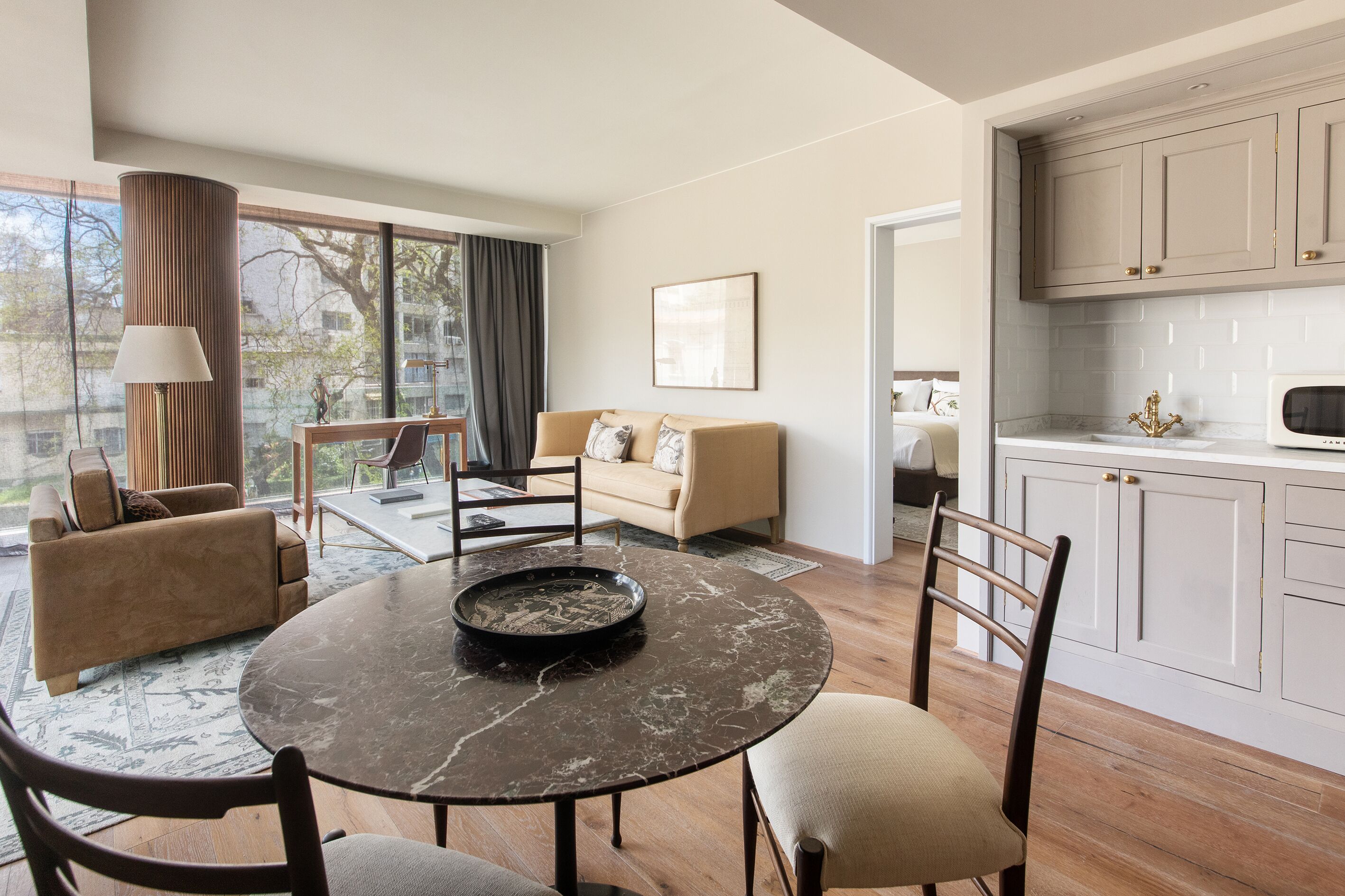 Una sala de estar moderna con una mesa redonda, un sofá color beige y una cocina con armarios blancos.
