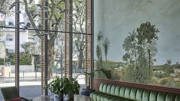 Una habitación amplia con un gran ventanal, un sofá verde, una mesa redonda con sillas y un techo decorativo con elementos colgantes.