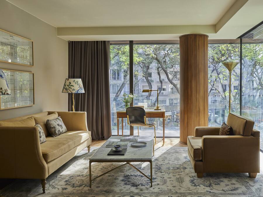 A modern living room with a sofa, armchairs, a coffee table, and a view of a cityscape through large windows.