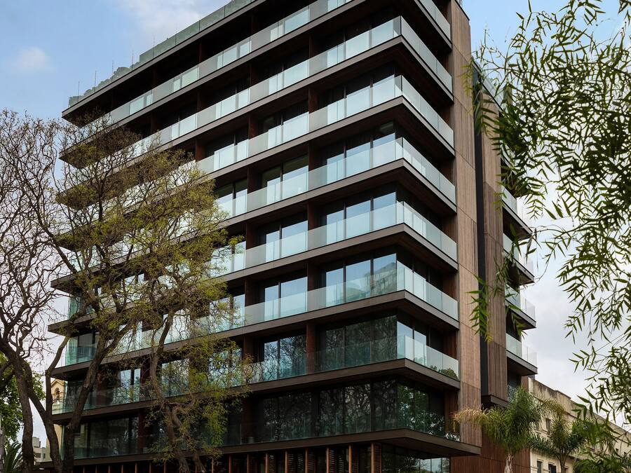 Un edificio de varios pisos con un diseño arquitectónico moderno, que combina elementos de fachada de vidrio y madera.