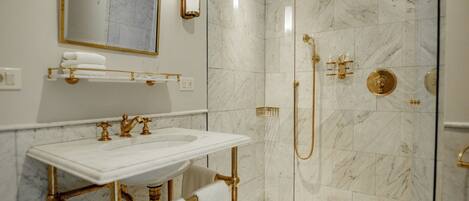 A bathroom with a marble sink, gold fixtures, and a glass-enclosed shower.