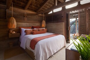 A bedroom with a large bed, wooden headboard, hanging lamps, and a view of the outdoors.