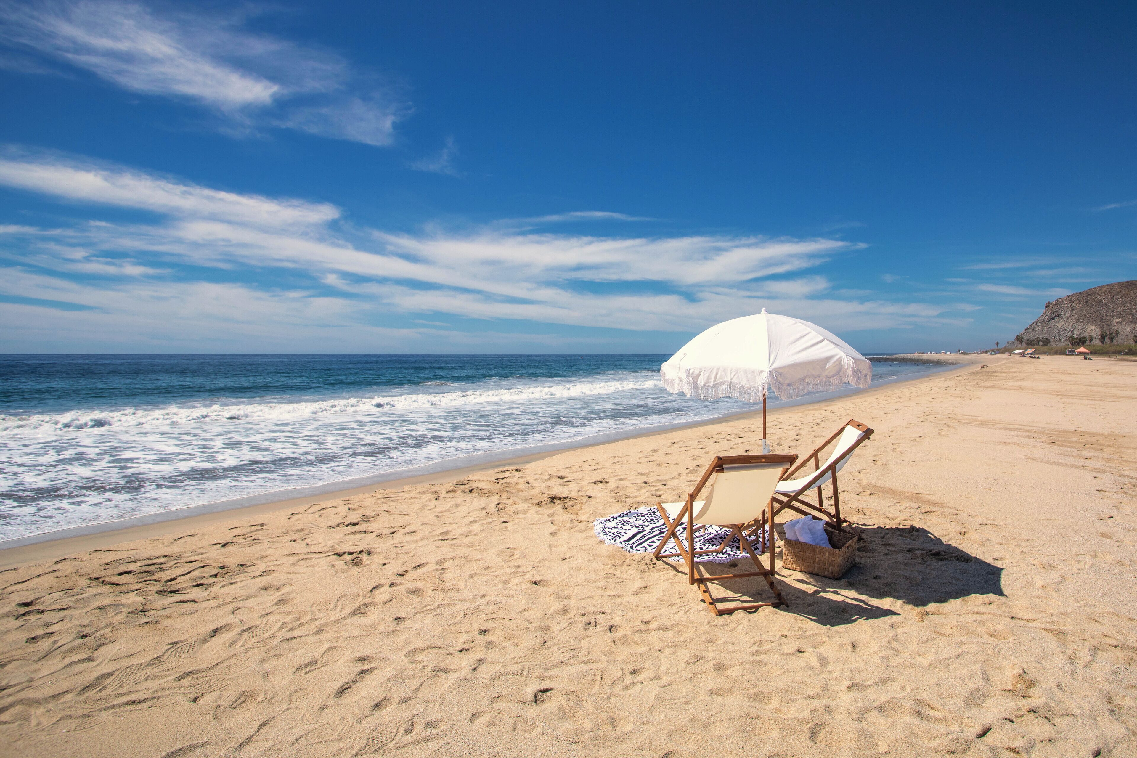 A beach with a single beach chair and umbrella, a rocky cliff in the background, and the ocean.