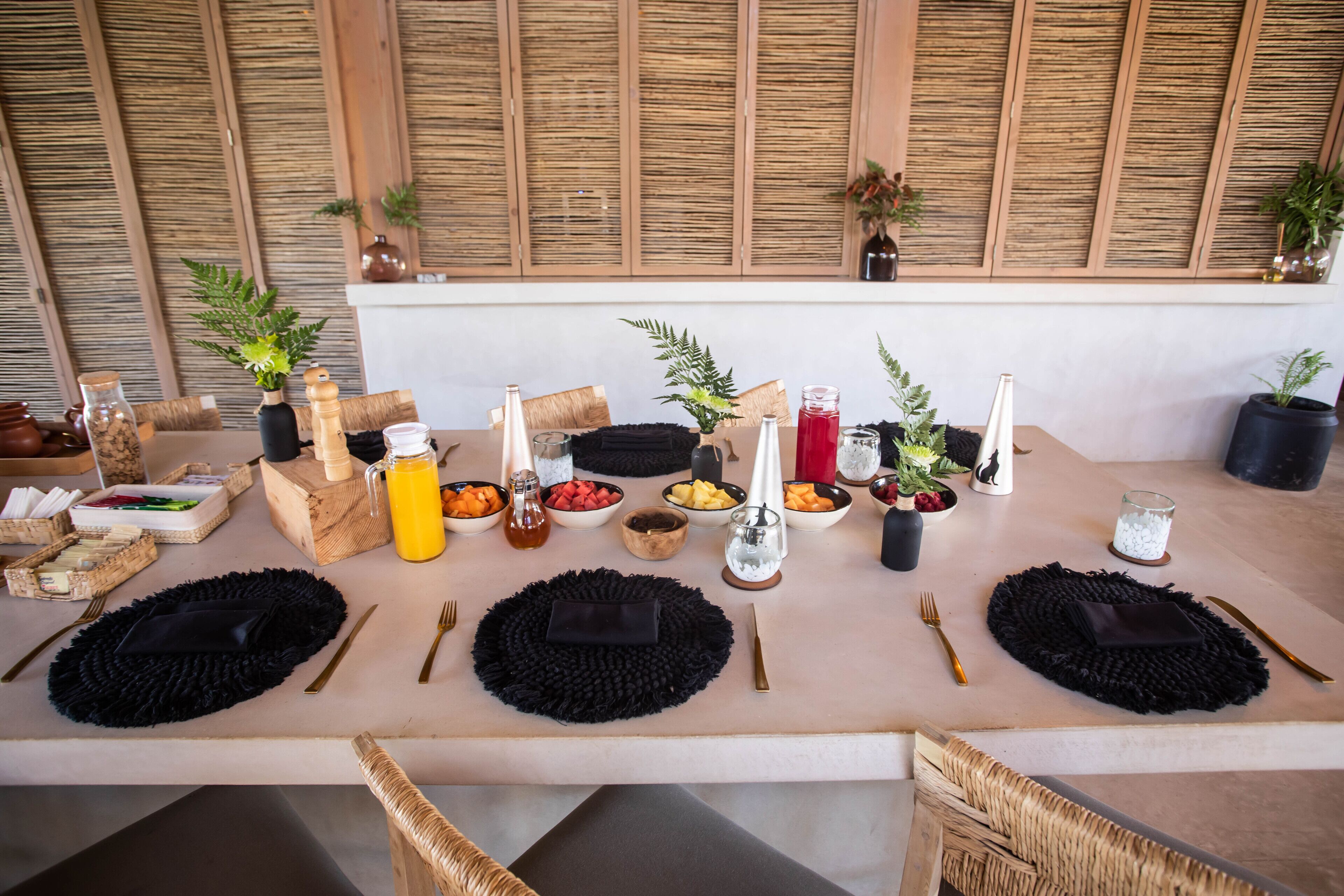 A dining table set with black placemats, gold cutlery, and various dishes and drinks.
