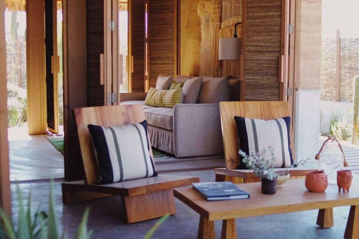 Ein moderner Sitzbereich im Freien mit Holzmöbeln und Kissen, einem Tisch mit Buch und Dekoration, und Blick auf die umliegende Landschaft.