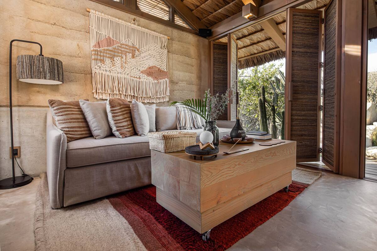 Ein modernes Wohnzimmer mit einem grauen Sofa, einem Holztisch und einer Wanddeko aus Makramee.