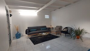 A modern living room with a grey sofa, a beige armchair, a coffee table, and a potted plant. - Le Ptit Gibs (Petit bourg)