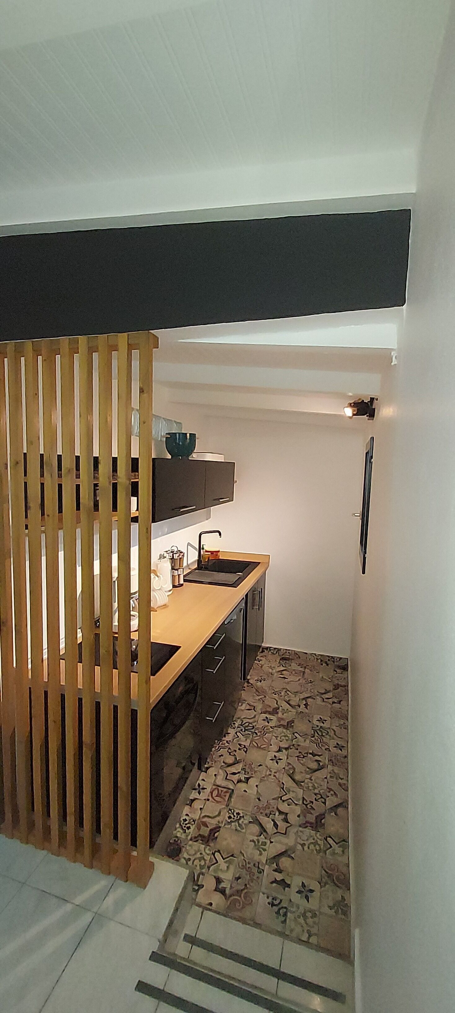 Une cuisine compacte avec un séparateur en bois, un évier et un sol à motifs.