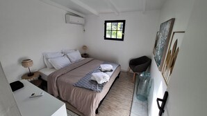 A bedroom with a bed, bedside tables, a window, a chair, a desk, and a wall-mounted air conditioner. - Le Ptit Gibs (Petit bourg)