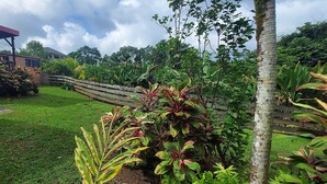 A well-maintained garden with a wooden fence, a covered structure, and lush greenery. - Le Ptit Gibs (Petit bourg)