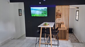 A modern room with a TV on the wall, a table with chairs, and a wooden partition. - Le Ptit Gibs (Petit bourg)