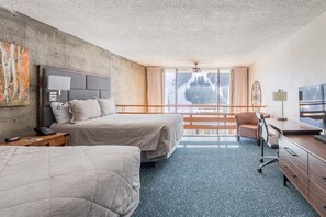 Ein Hotelzimmer mit zwei Betten, einem Schreibtisch, einem Sessel und einem Fernseher, mit Blick auf einen Berg.