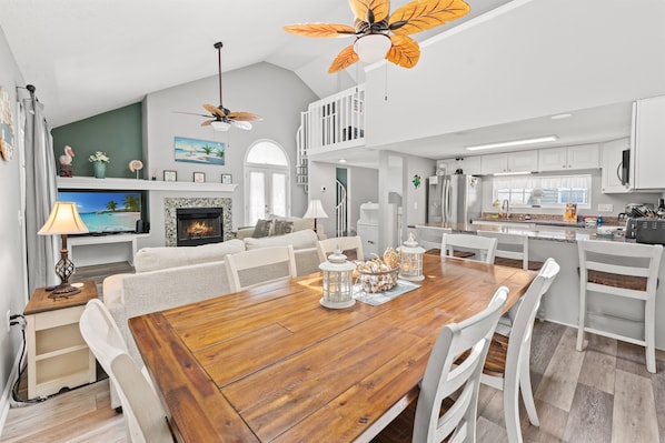 A spacious living area with a wooden dining table, white furniture, a fireplace, and a ceiling fan.