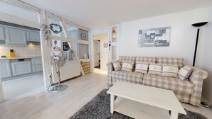 Ein Wohnzimmer mit einem karierten Sofa, einem weißen Couchtisch und einer Küchenzeile mit weißen Schränken und einer Heizung.