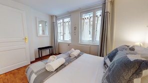 Une chambre d’hôtel avec un lit, un banc, un radiateur et une fenêtre avec des rideaux.