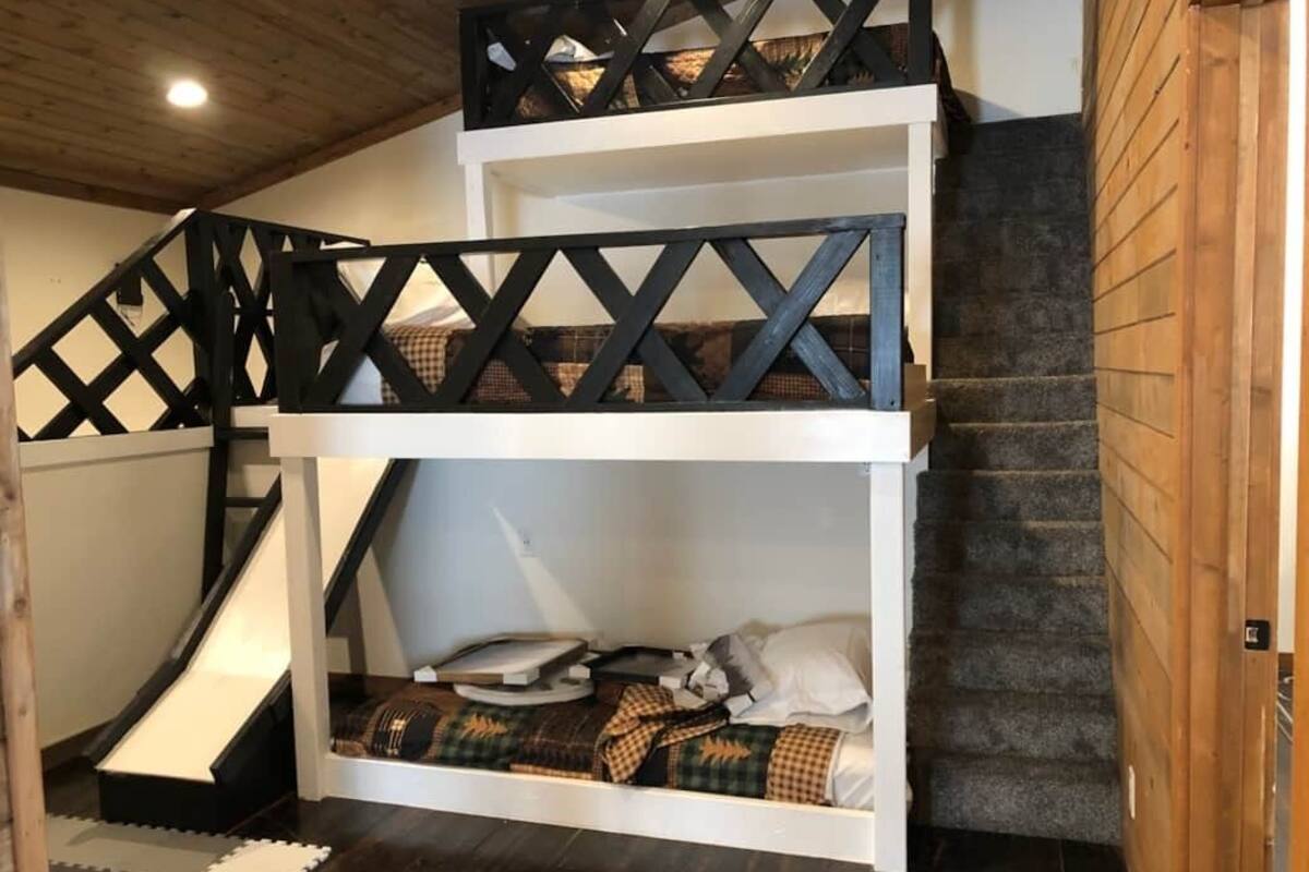 Un lit superposé avec une échelle, un petit bureau et un toboggan.