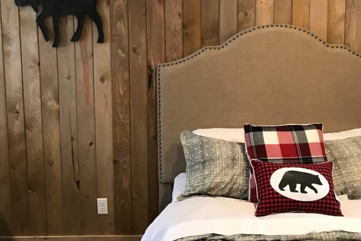 Une chambre avec des murs lambrés en bois, un lit avec une couette à carreaux et une décoration murale représentant un élan.