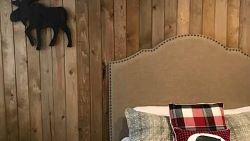 A bedroom with wooden panel walls, a bed with plaid bedding, and a moose wall decoration.
