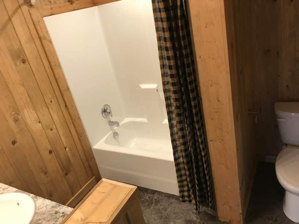 Un baño con piso de madera, una bañera blanca, un inodoro blanco y un banco de madera.