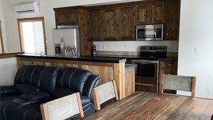 A modern kitchen with wooden cabinets, stainless steel appliances, and a black leather sofa.