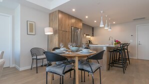 A modern kitchen with wooden cabinets, a stainless steel refrigerator, and a dining area with a round table and chairs. - Elegant Condo with Private BBQ and Ocean Views (Saanich North)
