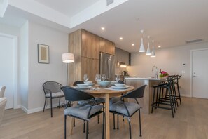 A modern kitchen with wooden cabinets, a stainless steel refrigerator, and a dining area with a round table and chairs. - Elegant Condo with Private BBQ and Ocean Views (Saanich North)