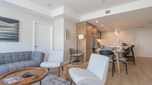 A modern living room with a grey sofa, a wooden coffee table, and a dining area with a table and chairs. - Elegant Condo with Private BBQ and Ocean Views (Saanich North)