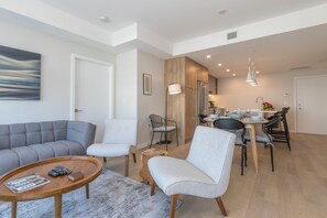 A modern living room with a grey sofa, a wooden coffee table, and a dining area with a table and chairs. - Elegant Condo with Private BBQ and Ocean Views (Saanich North)