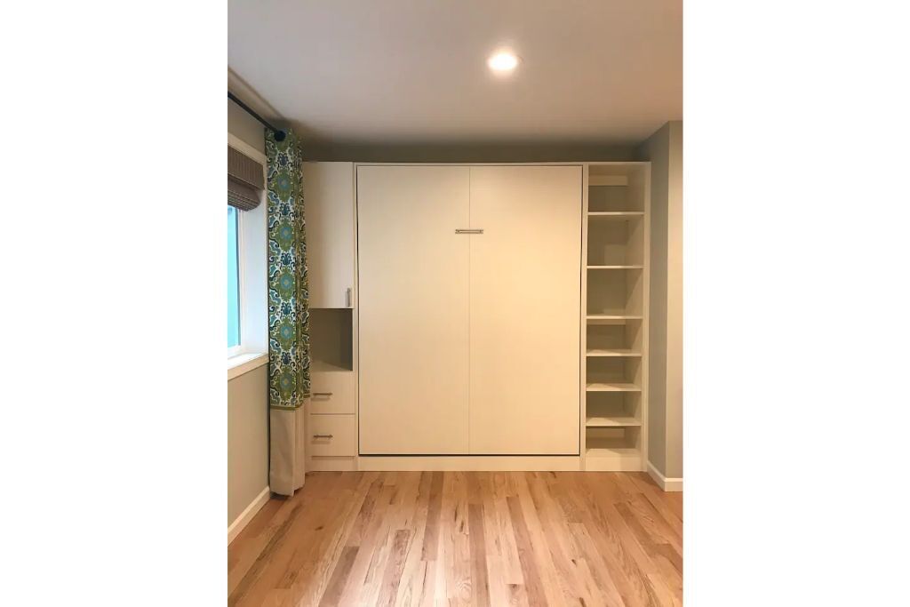 Una habitación con un armario grande, una ventana con cortinas estampadas y suelo de madera.